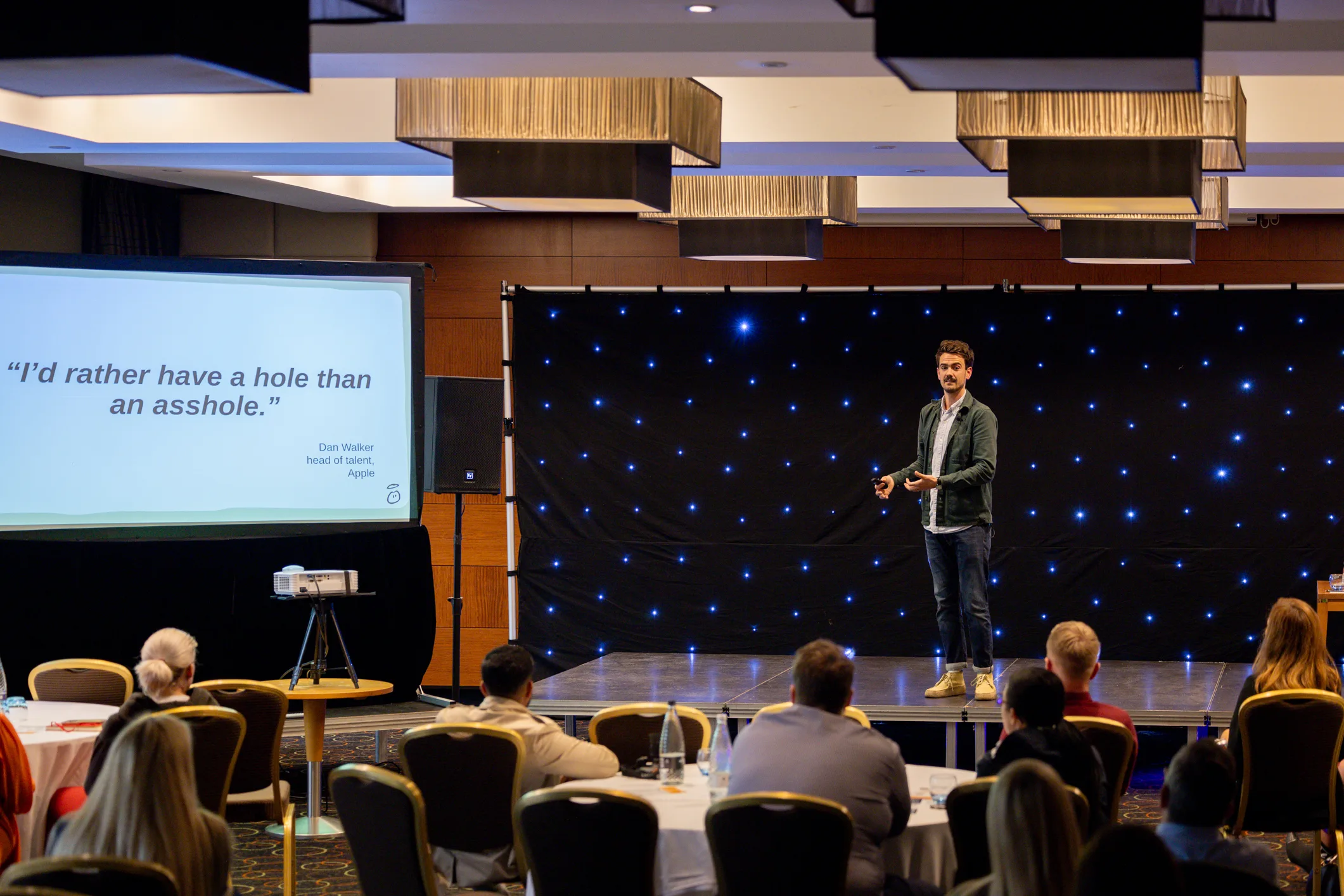 Wide view of a presenter on stage with event projection